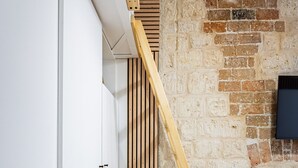 Une pièce avec un lit en mezzanine en bois, un mur en briques, une armoire blanche et un petit coin salon avec un coussin.