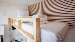 Un lit superposé avec une literie blanche, une tête de lit en lattes de bois et une étagère avec des verres et des bouteilles.