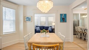 Ein Esszimmer mit einem Holztisch, weißen Stühlen, einem blauen Sofa und einem Chandelier.