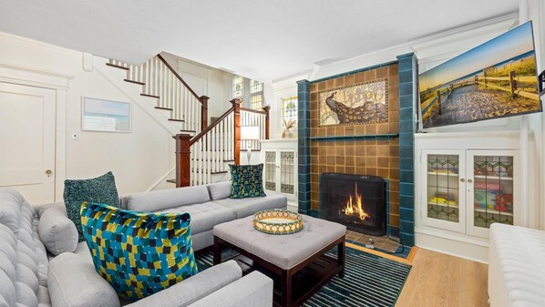 Ein Wohnzimmer mit Kamin, einer Treppe und einem Gemälde mit Strandmotiv.