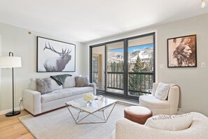 Ein modernes Wohnzimmer mit Sofa, Couchtisch und Sesseln, großen Fenstern mit Blick auf die Berge und Kunstwerken an den Wänden.
