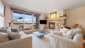 A living room with a stone fireplace, two sofas, a coffee table, and a large window with a view of mountains. - Luxury Amenities, Beaver Creek Ski-In/Ski-Out| LB403 (Beaver Creek)