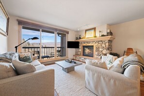 A living room with a stone fireplace, two sofas, a coffee table, and a large window with a view of mountains. - Luxury Amenities, Beaver Creek Ski-In/Ski-Out| LB403 (Beaver Creek)