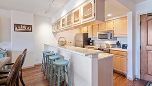 A kitchen with wooden cabinets, a central island with stools, a microwave, and a refrigerator. - Luxury Amenities, Beaver Creek Ski-In/Ski-Out| LB403 (Beaver Creek)