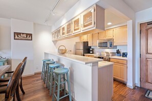A kitchen with wooden cabinets, a central island with stools, a microwave, and a refrigerator. - Luxury Amenities, Beaver Creek Ski-In/Ski-Out| LB403 (Beaver Creek)