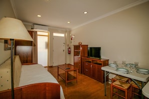 A hotel room with a bed, a desk, a television, and a dining table set for four. - FLH Monte Gordo Balcony Flat (Monte Gordo)