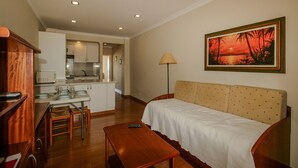 A hotel room with a kitchenette, a dining area, a sofa, and a painting on the wall. - FLH Monte Gordo Balcony Flat (Monte Gordo)