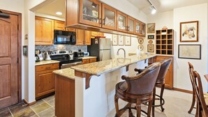 Una cocina con armarios de madera, encimeras de granito, un refrigerador, un microondas y una cafetera.