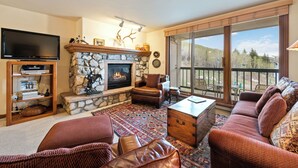 Una sala de estar con chimenea de piedra, muebles de cuero, un televisor de pantalla plana y un ventanal con vistas.