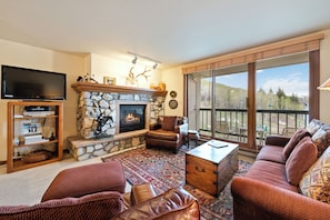 A living room with a stone fireplace, leather furniture, a flat-screen TV, and a large window with a view. - Luxury Amenities, Beaver Creek Ski-In/Ski-Out| LB405 (Beaver Creek)
