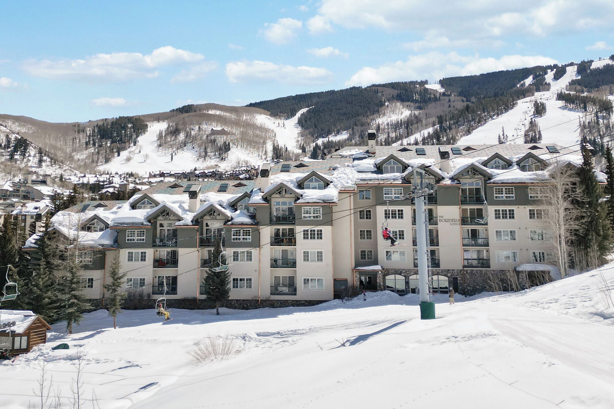 A multi-story hotel with a ski lift in the foreground, surrounded by snow-covered mountains.
