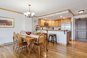 A modern kitchen with wooden cabinets, a stainless steel refrigerator, and a dining area with a wooden table and chairs.