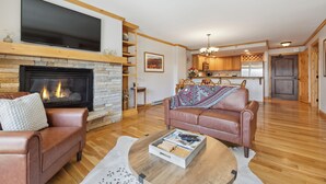 Ein Wohnzimmer mit Kamin, Ledersofas, einem Flachbildfernseher und einer Küche im Hintergrund.
