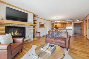 Ein Wohnzimmer mit Kamin, Ledersofas, einem Flachbildfernseher und einer Küche im Hintergrund.