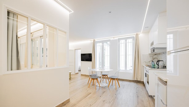 A modern kitchen with white cabinetry, a dining area with a round table and chairs, and large windows allowing natural light. - Cœur Batignolles-Europe-2 rooms-charm-Paris 8 (Paris)