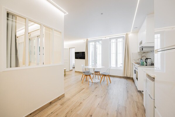 Eine moderne Küche mit weißen Schränken, einem Essbereich mit rundem Tisch und Stühlen sowie großen Fenstern für natürliches Licht.