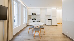 A modern kitchen with white cabinets, a microwave, and a washing machine. There is a dining area with a round table and chairs. - Cœur Batignolles-Europe-2 rooms-charm-Paris 8 (Paris)