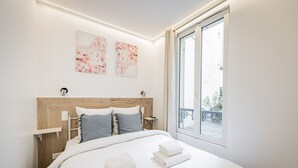 A bedroom with a wooden headboard, two bedside tables, a large window, and a view of the outside. - Cœur Batignolles-Europe-2 rooms-charm-Paris 8 (Paris)
