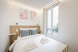 Ein Schlafzimmer mit einem hölzernen Kopfteil, zwei Nachttischen, einem großen Fenster und Blick ins Freie.