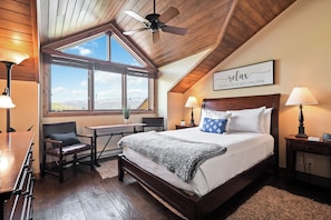 Ein Schlafzimmer mit einem großen Bett, einem Schreibtisch, einem Stuhl, einem Deckenventilator und einem Fenster mit Blick auf die Berge.