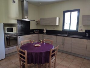 Eine Küche mit Esstisch, Stühlen, einer Mikrowelle, Backofen, Schränken und einem Fenster.