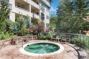 Ein Poolbereich mit Liegestühlen und einem Whirlpool, umgeben von Bäumen und einem Gebäude mit Balkonen.
