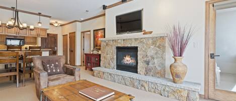 A living room with a fireplace, a television mounted above it, and a dining area with wooden furniture.