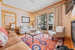 A living room with a sofa, armchair, coffee table, and a large window with curtains. - Beaver Creek Slope-Side Luxury | UB301 (Beaver Creek)