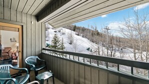 Un balcon donnant sur un paysage enneigé, avec des murs en bois et des chaises vertes.