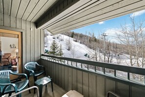 Ein Balkon mit Blick auf eine verschneite Landschaft, Holzwände und grünen Stühlen.