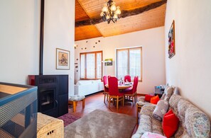 Ein gemütliches Wohnzimmer mit Kamin, einem Essbereich mit roten Stühlen und einem Sofa mit floralen Kissen.