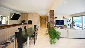 A modern kitchen with built-in appliances, a dining area with a glass table, and a living space with a TV and plants. - Luxury Lakeview Penthouse (Montagnola)
