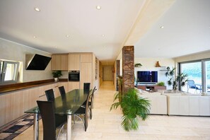 A modern kitchen with built-in appliances, a dining area with a glass table, and a living space with a TV and plants. - Luxury Lakeview Penthouse (Montagnola)