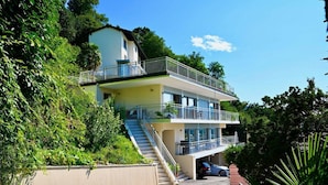 A two-story building with a balcony on the upper level, a staircase leading to the entrance, and a car parked in the driveway. - Luxury Lakeview Penthouse (Montagnola)