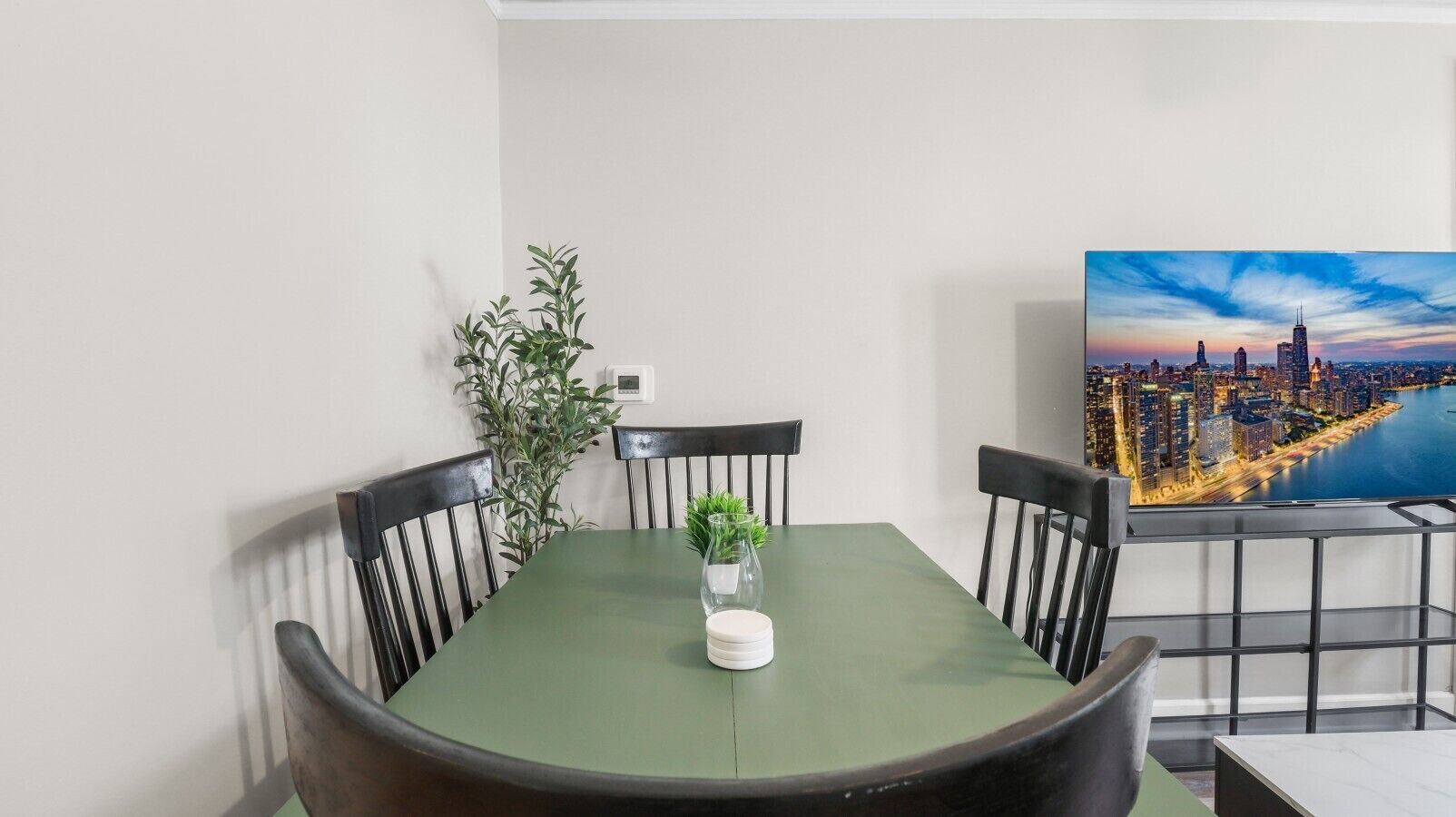 A dining area with a table, chairs, a potted plant, and a cityscape view.