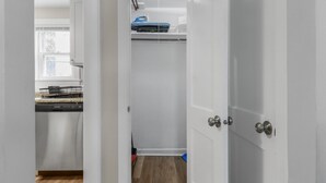 Un armari blanc amb porta, una zona de cuina amb rentavaixelles i una finestra.