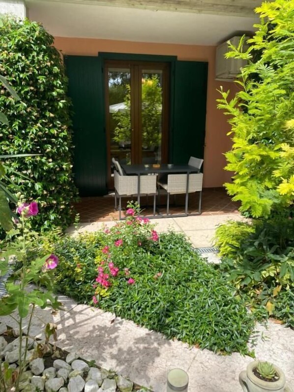 Un patio con mesa y sillas, rodeado de follaje y una planta en maceta.