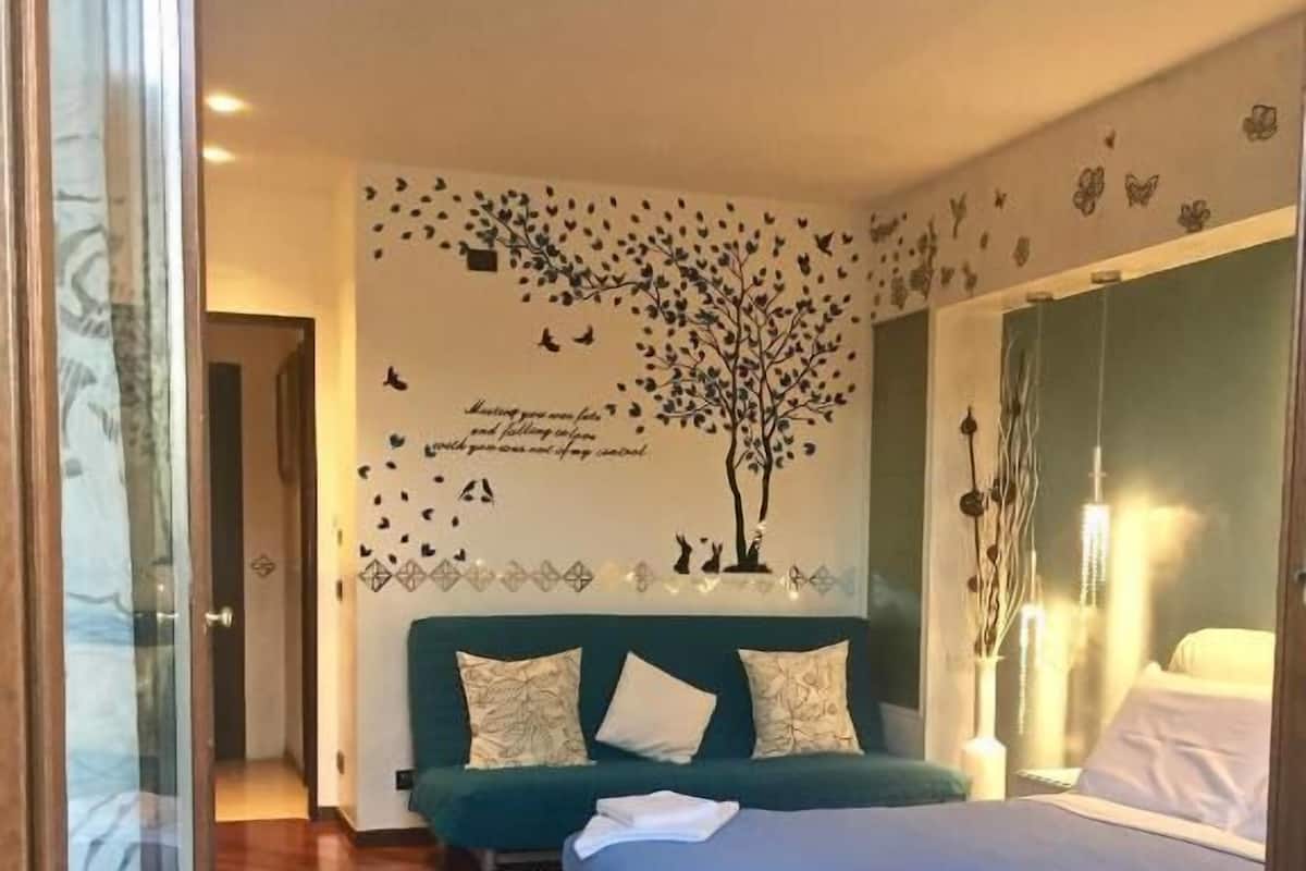 A bedroom with a bed, a green sofa, a decorative wall, and a patterned rug.