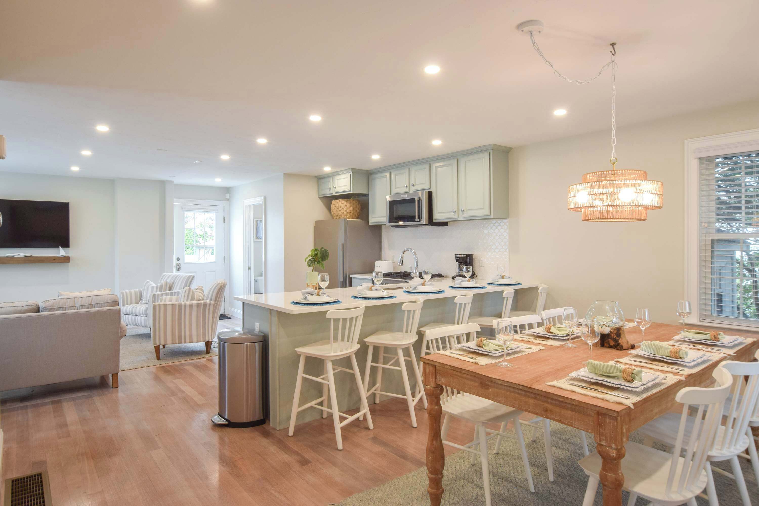 A modern kitchen with a central island, white bar stools, and a dining table set for six.