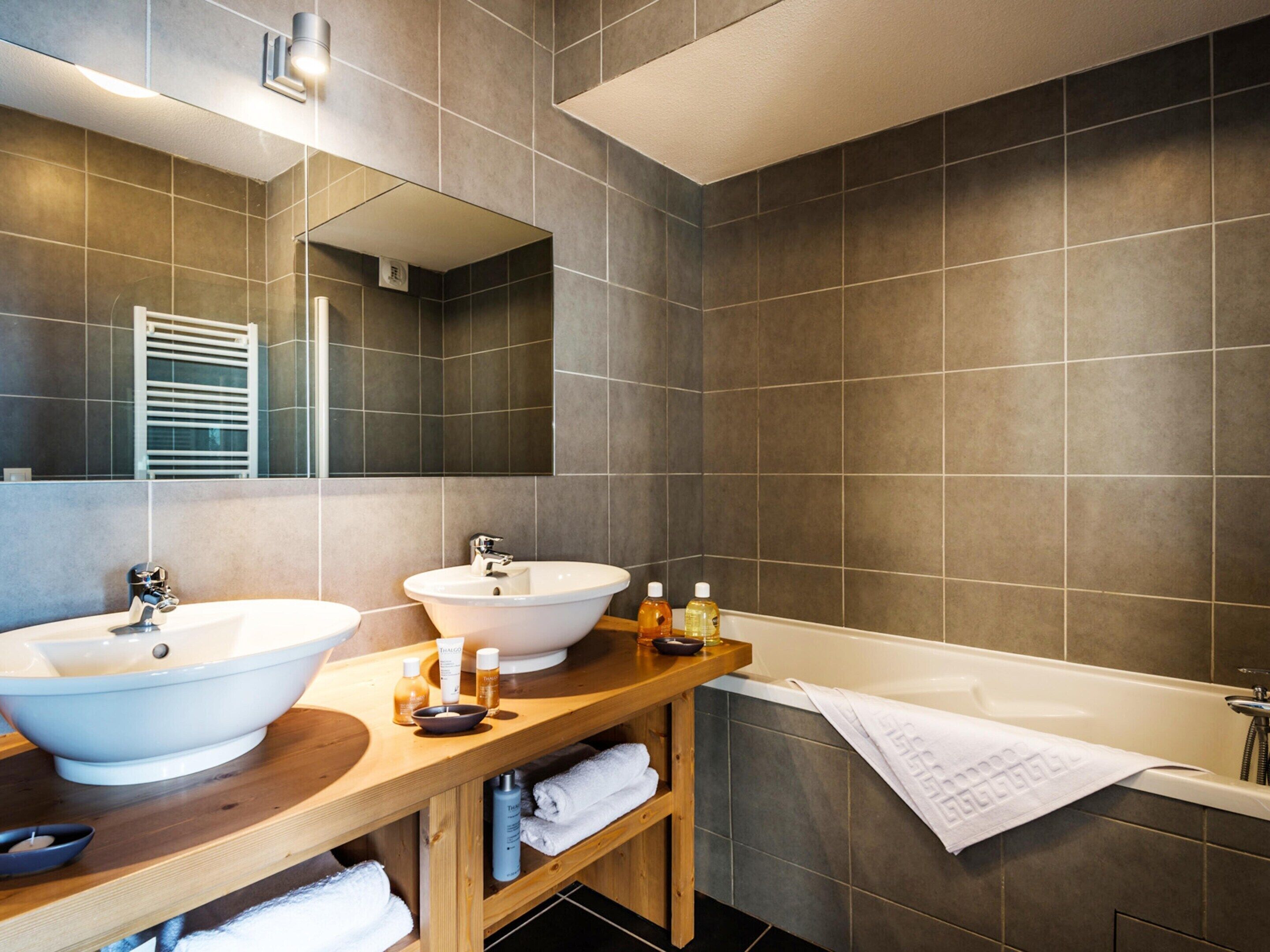 A modern bathroom with two sinks, a bathtub, and a wooden vanity.