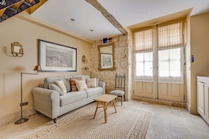 A living room with a sofa, a small table, a chair, a large window with curtains, and a stone wall. - A Sophisticated 1-BR - Saint-Germain (Paris)