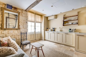 A compact kitchen with a dining area, stone walls, and a window with curtains. - A Sophisticated 1-BR - Saint-Germain (Paris)