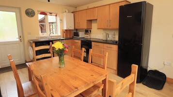 A kitchen with wooden cabinets, a black refrigerator, a dining table with chairs, and a vase with flowers.