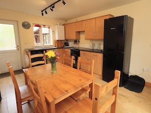 A kitchen with wooden cabinets, a black refrigerator, a dining table with chairs, and a vase with flowers. - Mellbeck Retreat (Kirkby Stephen)