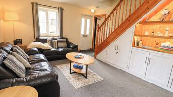 A living room with a black leather sofa, a wooden coffee table, a white cabinet with decorative items, and a wooden staircase.