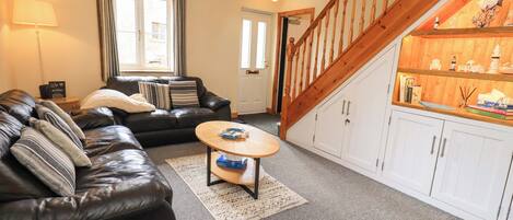 A living room with a black leather sofa, a wooden coffee table, a white cabinet with decorative items, and a wooden staircase.