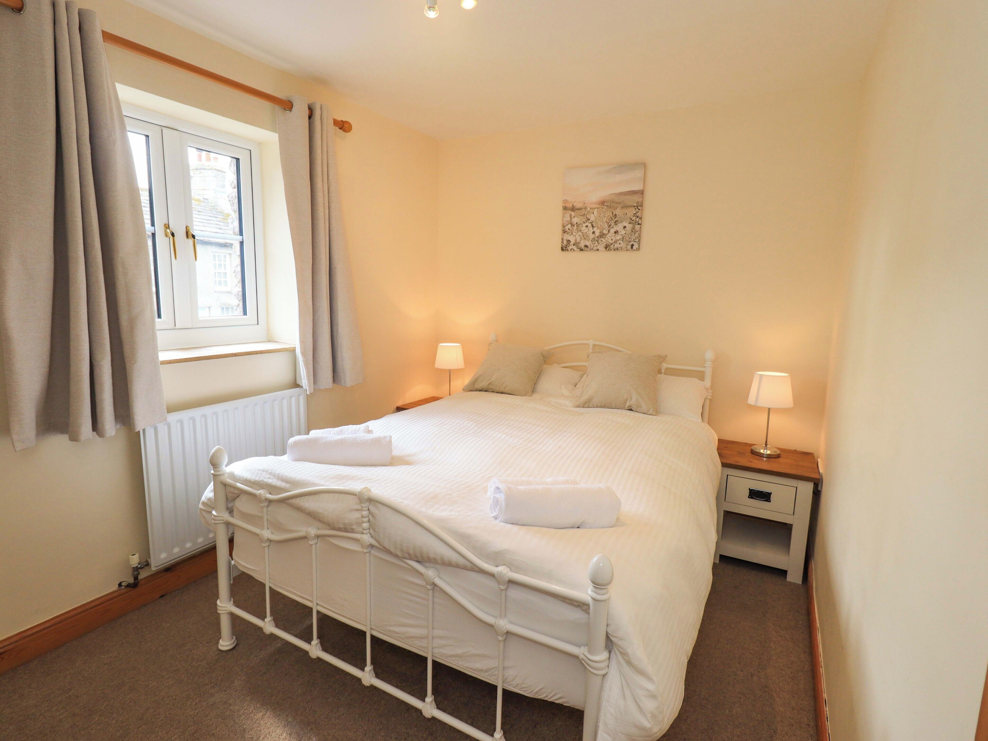 A neatly made bed with white linens, a bedside table with a lamp, and a window with curtains.