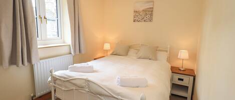 A neatly made bed with white linens, a bedside table with a lamp, and a window with curtains.