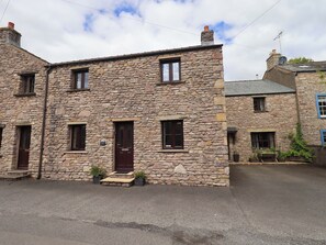 A stone building with a dark brown door, multiple windows, and a small front porch with potted plants. - Mellbeck Retreat (Kirkby Stephen)