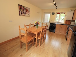 Un comedor con mesa y sillas de madera, una cocina con lavadora, y un cuadro en la pared.